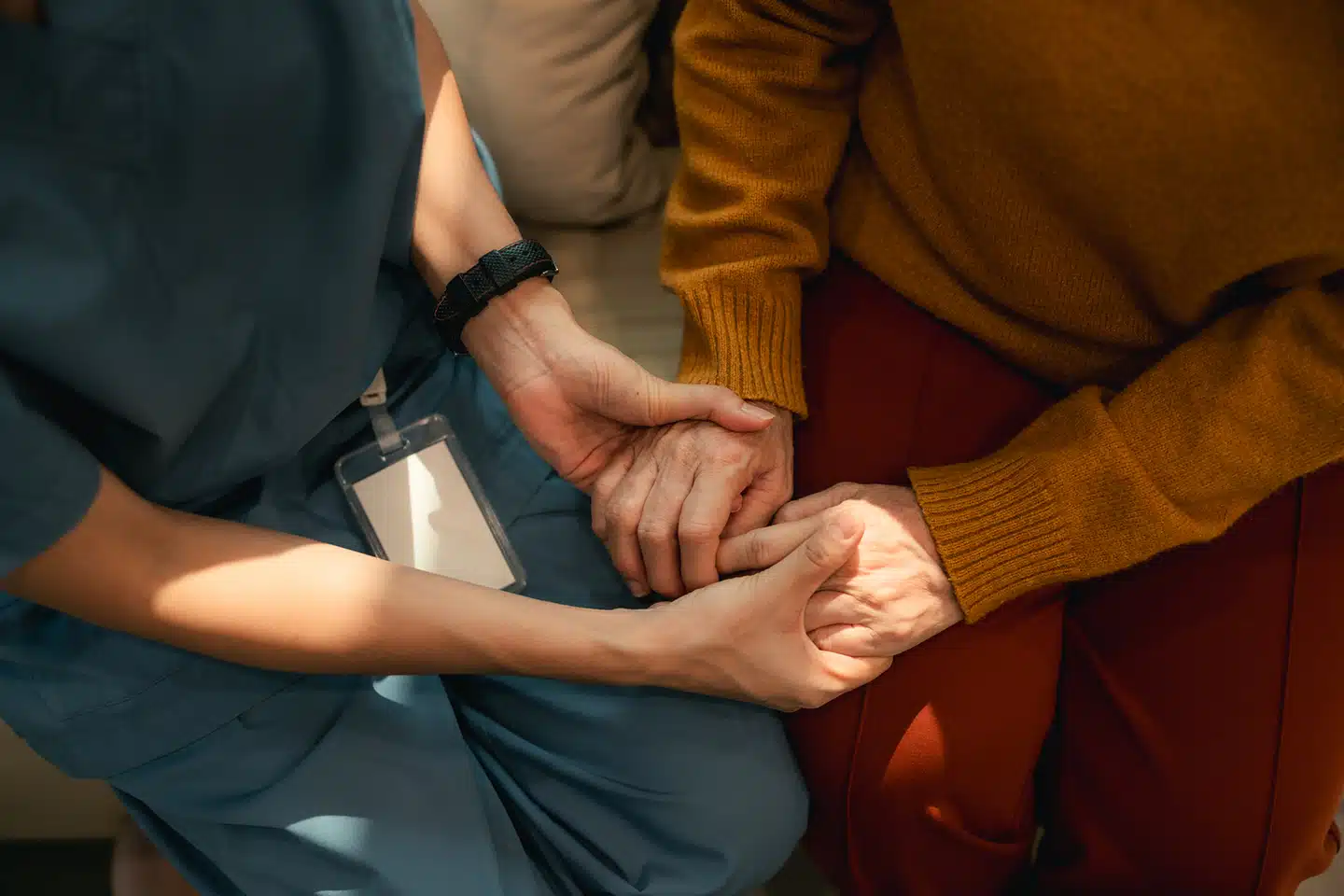 Nurse holding a client’s hands while providing in-home palliative nursing and comfort-focused support